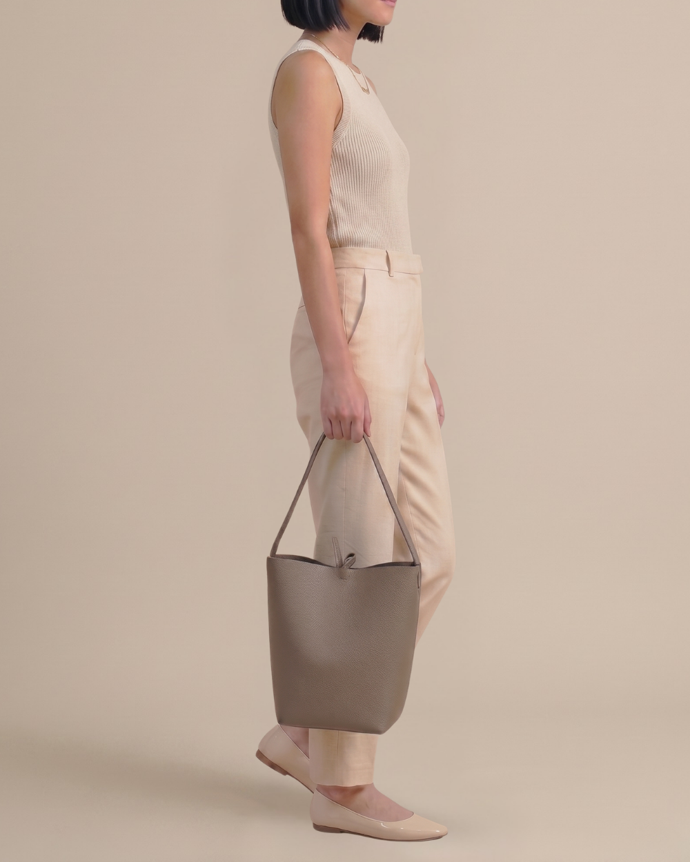 Woman carrying the Léa Bucket Bag in elephant gray pebbled cowhide, side profile, full body