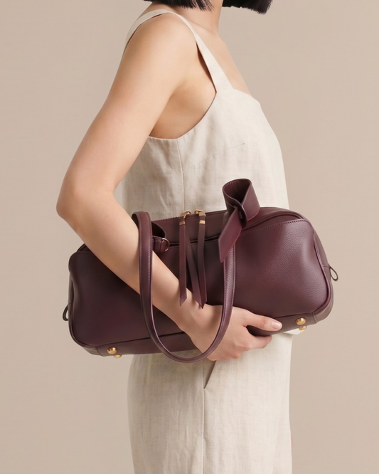 Woman carrying the Amélie Bowling Bag in wine red leather, showing half body